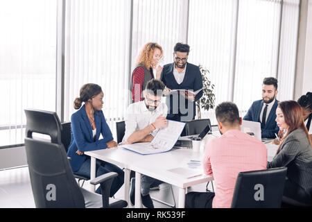 Rothaarige Frau Chef und ihr indischer männliche Assistent führenden Corporate Team Meeting präsentieren die Ziele von Teams in gut beleuchteten Konferenzraum Stockfoto