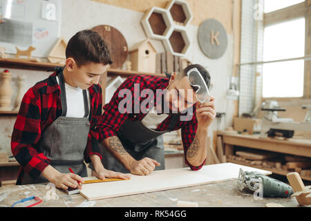 Neugierige kleine Junge Klassen der Tischlerei aus berühmten WOODWORKER. Hobby wächst in der Arbeit von Berufung. Stockfoto