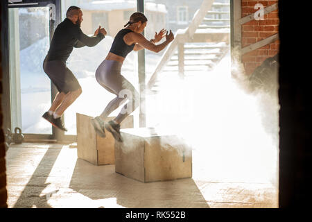 Kaukasische sportliche weibliche und männliche Sportler durchführen, springt auf und Fitnessraum mit Staub und Partikel in der Luft schweben Stockfoto