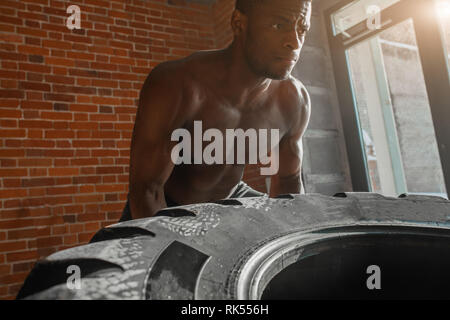 African American crossfit Mann bemüht sich zwar hart mit Hingabe und Entschlossenheit Anheben schwerer Reifen, Training von Kraft und Ausdauer Stockfoto