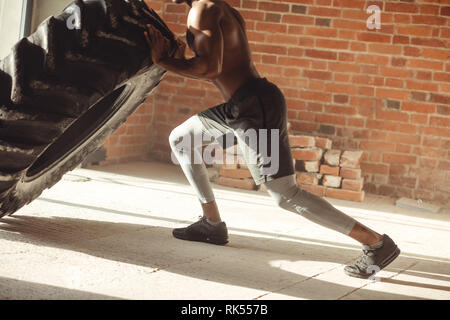 African American crossfit Mann bemüht sich zwar hart mit Hingabe und Entschlossenheit Anheben schwerer Reifen, Training von Kraft und Ausdauer Stockfoto