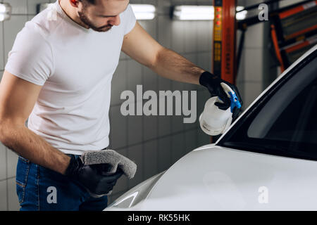 Ehrfürchtige junge Mann hält die Microfaser Tuch in der Hand und poliert die Auto, Job, Beruf, Beruf, bis schließen Foto Stockfoto