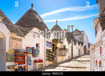 ALBEROBELLO, Apulien/ITALIEN - Zum 27. APRIL 2018: Trulli traditionelle apulische trockene Hütte aus Stein mit konischem Dach. Blick auf die Straße und traditionelle Souvenirläden. Stockfoto