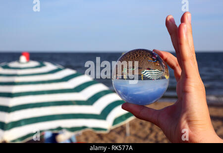Boy's Hand mit grossen Crystal Ball am Strand mit einem Sonnenschirm am Meer im Sommer Stockfoto