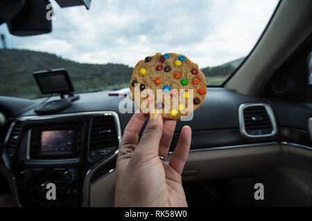 4. AUGUST 2016 - LOS ANGELES, Kalifornien: eine Hand hält eine bunte Chocolate Chip Cookie zu Essen während der Fahrt im Auto auf einem Road Trip, in LA t klemmt Stockfoto