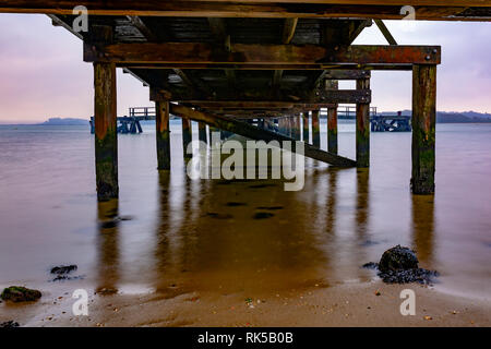 Landschaft Foto unter Lake Drive Pier ab Shoreline unter bewölktem Himmel auf einer inneren Hafen Strand, Poole, Dorset. Mit Langzeitbelichtung, die Stockfoto