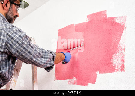 Kaukasische Haus Maler Arbeiter auf einem metallischen Leiter, mit der Walze er malt die Wand mit den farbigen Anstrich von Pink. Bauindustrie. Unten Stockfoto