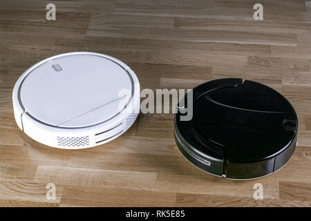 Problem der Auswahl Konzept. Zwei verschiedene Roboter Staubsauger Modelle Reinigung Staub auf Laminatböden. Moderne Reinigungstechnik housekeep Stockfoto