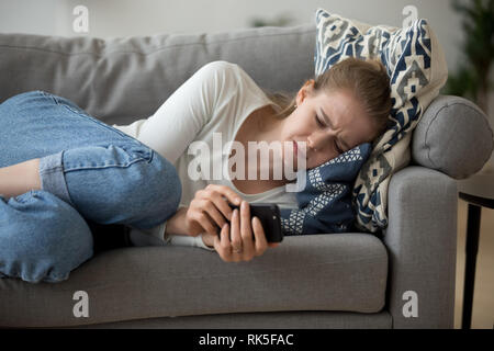 Verärgert junge Frau weinend auf der Couch liegend Holding Telefon besorgt Stockfoto