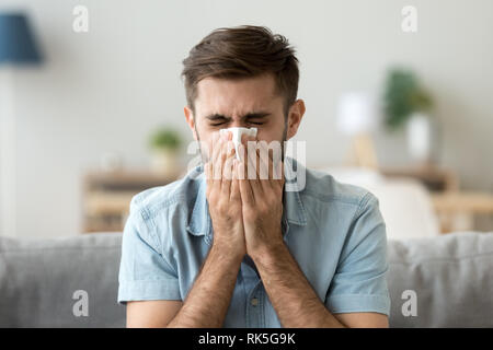 Kranke junge Mann Niesen in Taschentuch blasen Abwischen laufende Nase Stockfoto