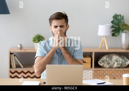 Krank am Arbeitsplatz junge Mann Grippe Niesen blasen Nase Stockfoto