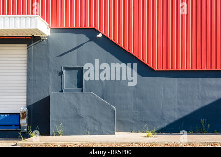 Ein fussgänger Tür in der Wand einer großen Lagerhalle, an der Spitze einer kleinen Treppe, unter einer rot Wellblech Abstellgleis mit einer Überwachungskamera. Stockfoto