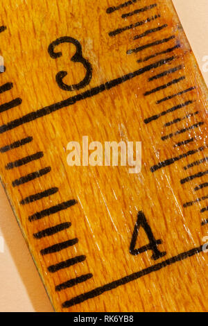 Nummer drei und vier auf einem gelben Holz- Lineal, schwarze Linien entlang der Kanten, der Herrscher verschlissen ist Stockfoto