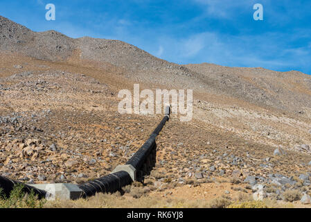 Schwarz Pipeline bis Wüste Berg Seite unter strahlend blauen Himmel mit weißen Wolken. Stockfoto