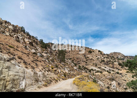 Unbefestigte Straße durch die Wüste Berge führen mit Berghang auf links und rechts unter dem blauen Himmel mit Wolken. Stockfoto