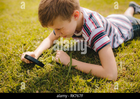 Kaukasischen jungen erkunden Garten Gras mit seiner Lupe. Junge durch die Lupe am Gras suchen. Stockfoto