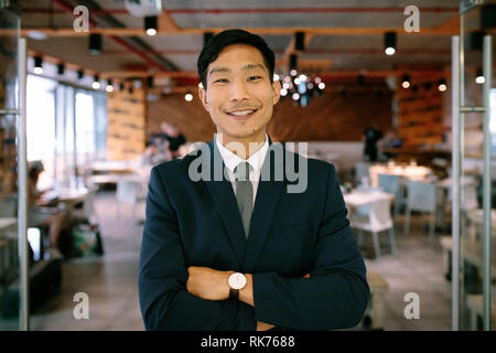 Portrait von selbstbewussten jungen Geschäftsmann an Coffee Shop. Asian Business Mann stand mit verschränkten Armen und Kamera. Stockfoto