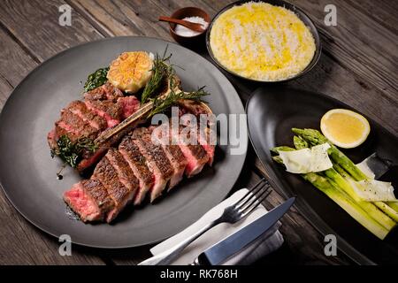 Köstliches und saftiges T-Bone Steak in Scheiben, serviert mit Spargel, rasierten Käse und Kartoffelpüree Stockfoto
