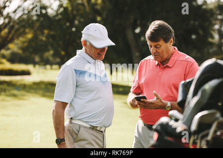 Ältere Menschen unter Bruch von Golf und mit Handy. Reifer Mann zeigt die Punktzahl zu seinem Freund nach dem Spiel auf den Golfplatz. Stockfoto