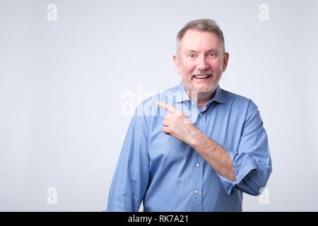 Happymature Kerl im blauen Hemd an Kamera suchen, lächelnd und zur Seite hin Stockfoto