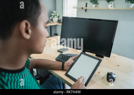 Portrait der junge Unternehmer mit einem Tablet viele Art von Ihrem Geschäft sitzen vor monitor Computer im Zimmer zu handhaben Stockfoto