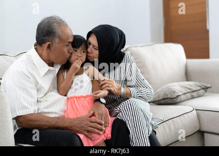Großeltern kiss Enkelin auf ein Küken beim Sitzen auf einer Couch Stockfoto