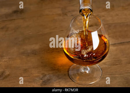 Brandy in das Glas gießen. Auf Holztisch Cognac Stockfoto