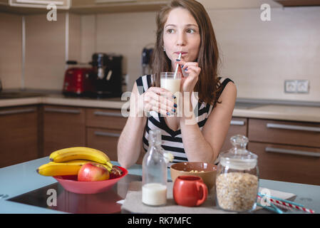 Frau trinkt organische Hafermilch aus Strohhalmen halten ein Glas Glas Schale in der Küche. Flasche und Obst auf den Tisch. Ernährung Gesunde vegetarische Produkt Stockfoto