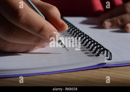 Tausendjährige Frau schriftlich in einer Spirale gebundenes Notizbuch, Stift in der Hand Stockfoto