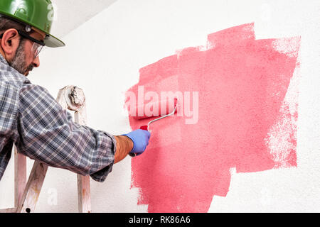 Kaukasische Haus Maler Arbeiter auf einem metallischen Leiter, mit der Walze er malt die Wand mit den farbigen Anstrich von Pink. Bauindustrie. Unten Stockfoto