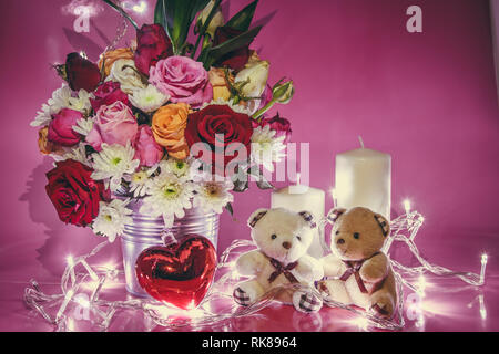 Vase Bouquet Rosen in Aluminium Schaufel und Rot funkelnden Herzen. Paar schöne Bären sitzen in der Nähe von white Kerzenständer auf rosa Hintergrund. Leuchten Licht Stockfoto