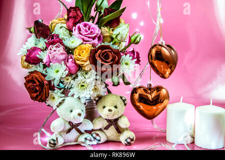 Paar schöne Bären sitzen in der Nähe von Bouquet Rosen in Vase Aluminium Schaufel und Rot glitzernden Herz mit weißen Kerzenständer auf rosa Hintergrund. Valentine da Stockfoto