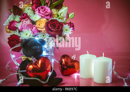 Vase Bouquet Rosen in Aluminium Schaufel. Teddy Bear mit roten Herzen und weiss glitzernde Leuchter auf rosa Hintergrund. Leuchtet das Licht der Liebe in Stockfoto