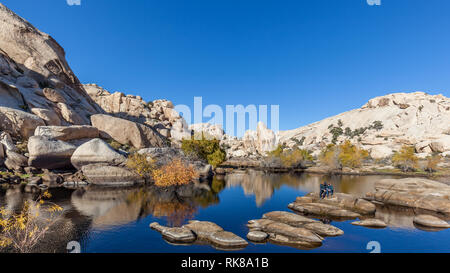 Ein Männer und Frauen sitzen auf dem Rock am Patientenbett Wasser an der Barker Dam (Big Horn Dam) in Joshua Tree National Park in Kalifornien. Stockfoto