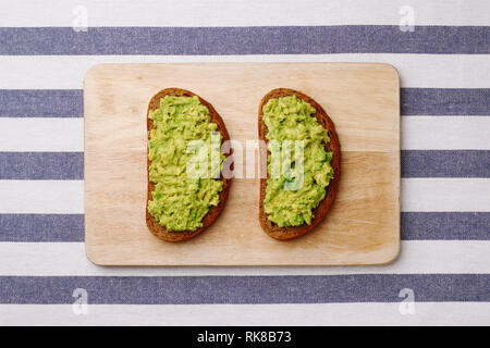 Guacamole Sandwich auf hellen Hintergrund. Avocado Sandwiches auf Holzbrett und textile Draufsicht Stockfoto