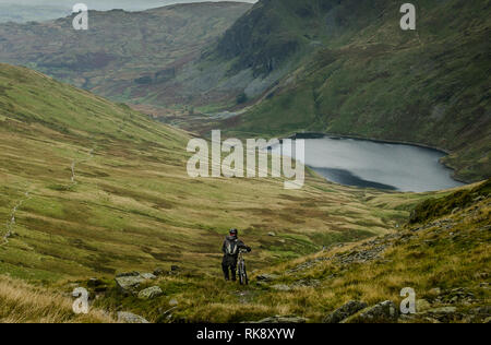 Ein Single Mountain Biker zu Fuß sein Fahrrad auf einem Hügel mit einem kleinen See in der Nähe Haweswater, Lake District, England Stockfoto