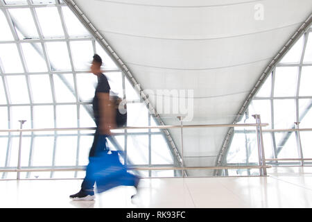 Ein Mann in Bewegungsunschärfe auf weißen Flur mit großen Fenstern. Verschwommene Menschen zu Fuß in einem modernen Gebäude. Abstraktes Bild von Reisenden im lobb Stockfoto