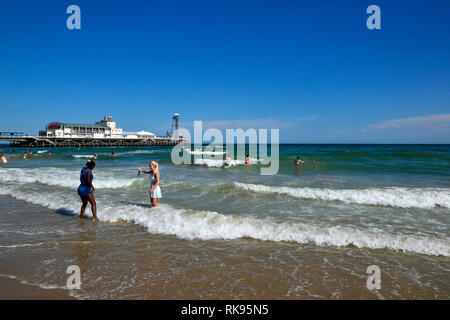 Zwei junge Frauen, Schwarz und Weiß, im Meer vor Bournemouth Pier, Bournemouth, England, Großbritannien Stockfoto