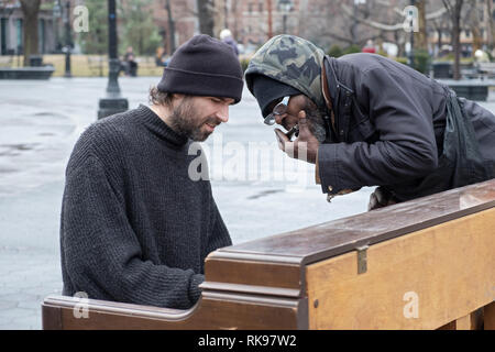 Ein Klavier spielen Gaukler führt mit einem Passanten bye Wer hat blues Duette mit ihm auf seiner Mundharmonika. Im Washington Square Park in Manhattan, New York City. Stockfoto