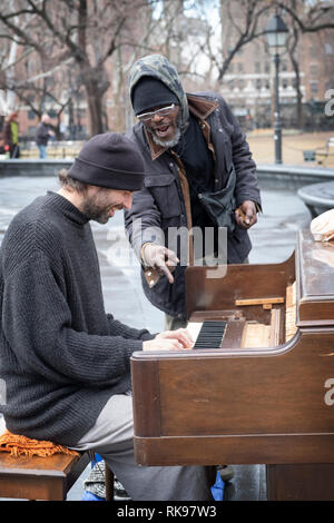 Ein Klavier spielen Gaukler führt mit einem Passanten bye Wer hat blues Duette mit ihm auf seiner Mundharmonika. Im Washington Square Park in Manhattan, New York City. Stockfoto