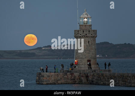 Vollmond hinter Herm Insel mit Guernsey breakwater Leuchtturm im Vordergrund steigende Stockfoto