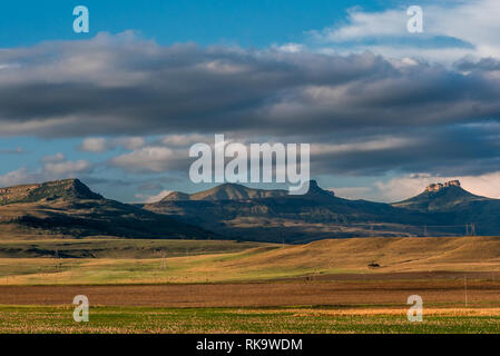 Das Amphitheater und die umliegenden Berge unter einem blauen und bewölkter Himmel mit einem Tal der bunten Ebenen bis in den späten Abend Sonne beleuchtet. Drakensberge, S Stockfoto