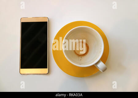 Mit einer leeren Tasse von fertigen Kaffee trinken am weißen Tisch isoliert Smartphone Stockfoto