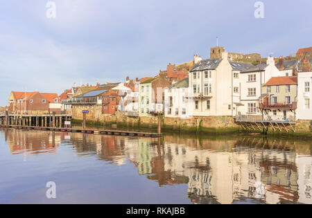 Gebäude entlang der Uferpromenade am Whitby im Wasser des Hafens wider. Einem Hügel überragt die Häuser mit einer Kirche auf dem Gipfel. Stockfoto