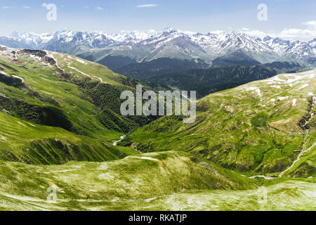 Atemberaubend schöne fabelhafte Aussicht auf grünen Hügeln und Gräser gegen die hohen schneebedeckten Felsen auf den blauen Himmel und Wolken. Der Сoncept dventure und Hi Stockfoto