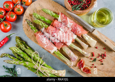 Frische organische Spargel in Schinken auf einem Schneidebrett gewickelt. Stockfoto