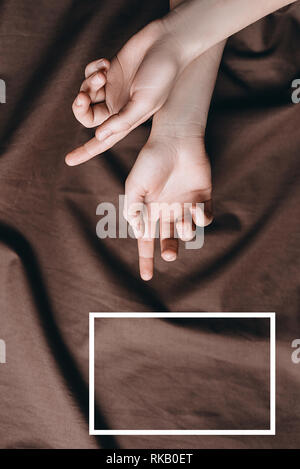 Weibliche Hände vor dem Hintergrund der Braun Stoff mit einem gezeichneten weißen Rahmen. Minimale kreative abstraktes Konzept. Flach. Kopieren Sie Platz für Text Stockfoto