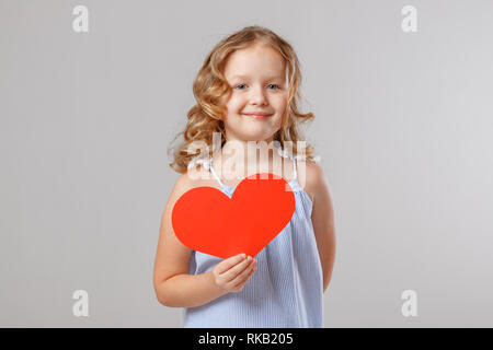 Portrait einer entzückenden kleinen Kind Mädchen hält ein rotes Herz aus Papier. Grauer Hintergrund, Studio Stockfoto