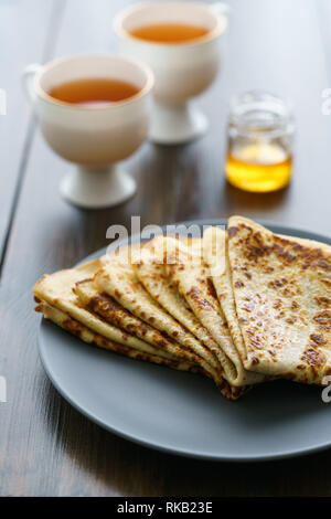 Crepes auf einem grauen Keramik Teller serviert mit Honig und 2 Tassen Kaffee. Dunkler Holztisch, hohe Auflösung Stockfoto