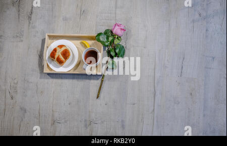 Flachbett Top Shot eines Fachs mit Zitrone, Kaffee und Hot Cross bun. Eine schöne Single rosa Rose Stammzellen neben liegen. Auf einem Dritten mit Copyspace thi gelegen Stockfoto